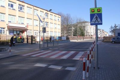 Na zewnątrz, dzień. Przejście dla pieszych biało-czerwone. Po lewej budynek szkoły