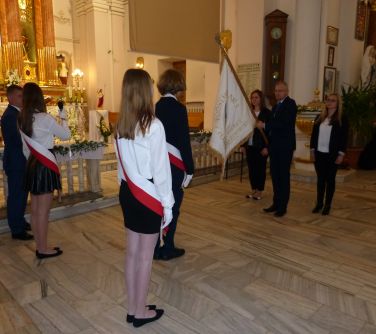 Wnętrze kościoła. Osoby przekazują sztandar młodszym ubranym na galowo dzieciom