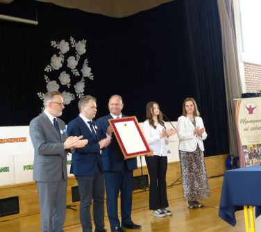 Jasna aula. Trzech mężczyzn. trzymają obraz. Po prawej dwie kobiety