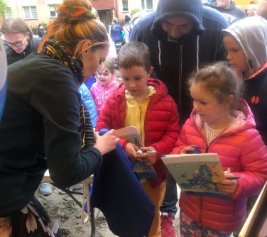 Na zewnątrz. Kobieta coś pokazuje zgromadzonym osobom
