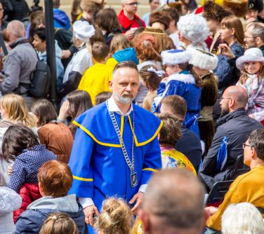Słoneczny dizeń. Pomiędzy zgromadzonymi osobami stoi mężczyzna w niebieskiej todze