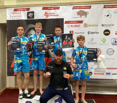 czterech zawodników MMA na podium pozuje do zdjęcia z trenerem