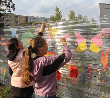 dziewczynki malują na folii rozciągniętej między drzewami