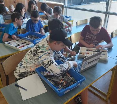 grupa dzieci podczas zajęć z robotyki siedzi przy ławkach