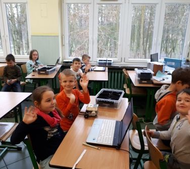 grupa dzieci podczas zajęć z robotyki macha do zdjęcia