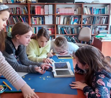 grupa dziewczynek pochyla się nad granatowym brystolem z naklejonymi gwiazdkami