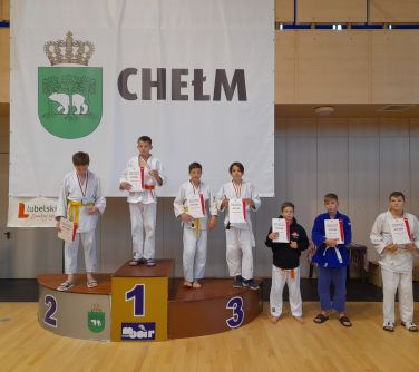 Grupa młodych zawodników judo na podium, w tle baner z napisem "Chełm"