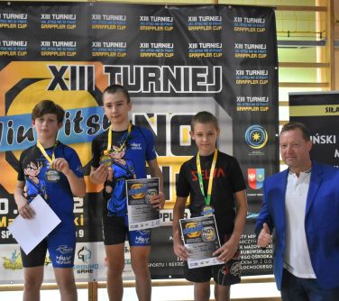 trzech zawodników pozuje do zdjęcia na podium w towarzystwie mężczyzny