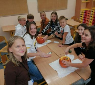 uśmiechnięci uczniowie przy stolikach wydrążają dynie