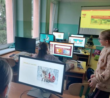 widok na salę zajęciową, w tle ekran, na pierwszym planie monitory komputerowe z motywem świątecznym
