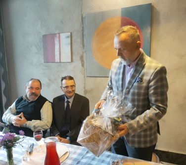 dwóch mężczyzn siedzących przy stole w towarzystwie burmistza miasta trzymającego w rękach upominek