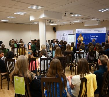 zgromadzona młodzież na spotkaniu, na drugim planie kobieta przemawia do mikrofonu