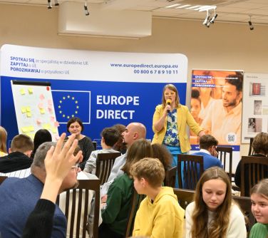 uczestnicy spotkania, na drugim planie kobieta przemawia do mikrofonu