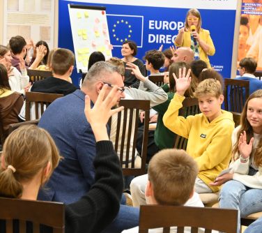 uczestnicy spotkania, na drugim planie kobieta przemawia do mikrofonu