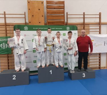 młodzi zawodnicy judo na podium w towarzystwie trenera