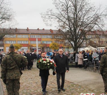 mężczyźni składają wiązankę pod pomnikiem niepodległości