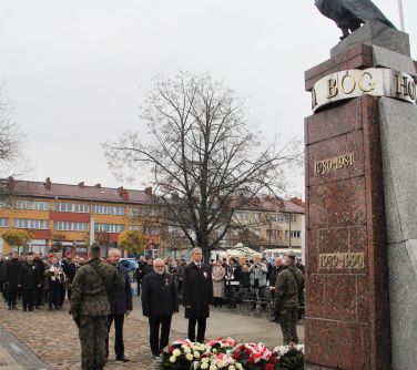 mężczyźni składają wiązankę pod pomnikiem niepodległości