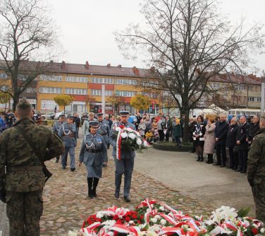 kobieta i mężczyzna w mundurach składają wiązankę pod pomnikiem niepodległości