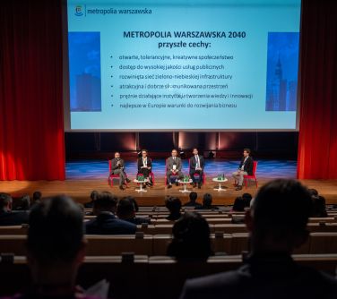 prelegenci siedzacy na scenie, w tle napis Metropolia Warszawska, widok z publiczności