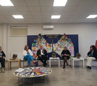 debata, osoby siedzą na krzesłach , mężczyzna mówi do mikrofonu