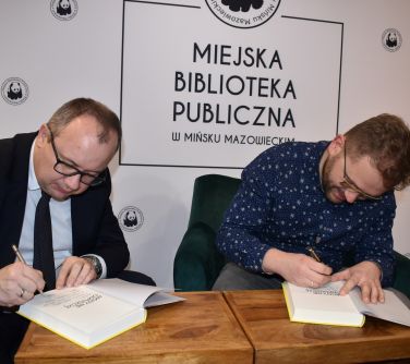 dwóch mężczyzn siedzi, podpisują książki