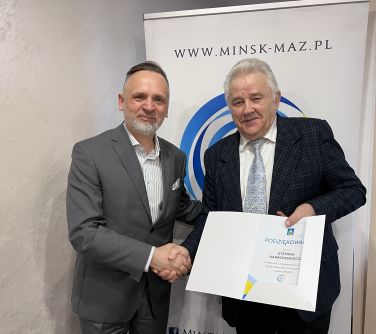 mężczyzna pozuje z mężczyzną, mężczyzna trzyma otwartą białą teczkę w dłoni, w tle baner