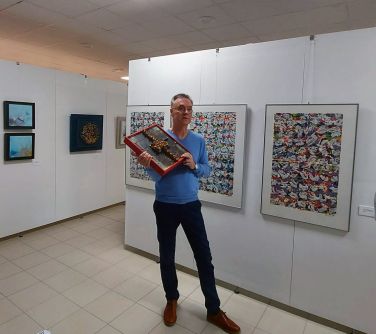mężczyzna stoi na korytarzy trzyma obraz w rękach, na białych ścianach wiszą obrazy