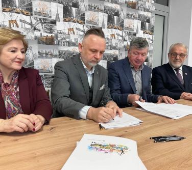 cztery osoby siedzą przy stole kobieta i trzech mężczyzn, jeden z mężczyzn podpsiuje dokumenty