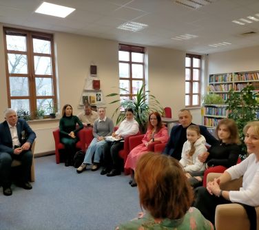 osoby siedzą w czerwonych fotelach w półokręgu