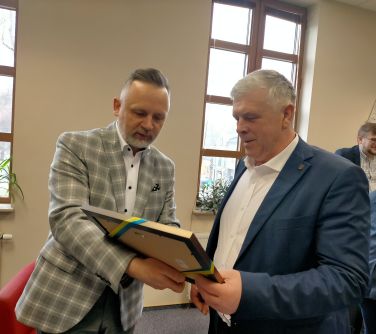 mężczyzna wręcza stojącemu obok drugiemu mężczyźnie obrazek