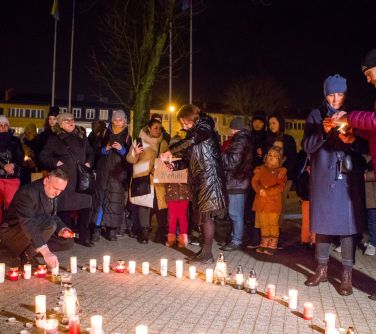 koło ułożone ze świec naokoło ludzie zapalający kolejne świecie