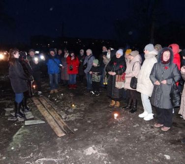 ludzie stoja w półkolu niektórzy trzymają czerwone goździki