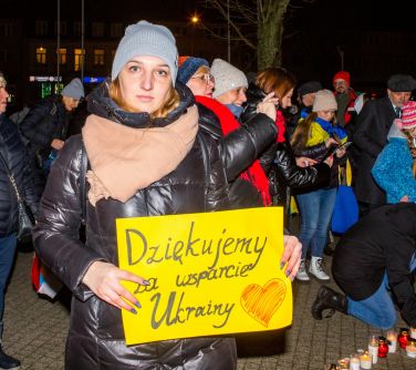 osoby stoją, jedna kobieta pozuje do zdjęcia trzymając w rekach transparent Dziękujemy za wsparcie ukrainy