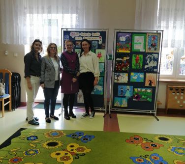 trzy kobiety pozuja do zdjęcia, stoją przy dwóch tablicach z pracami dzieci