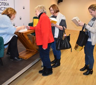 kobieta siedzi w fotelu podpisuje książki, osoby podchodzą do niej