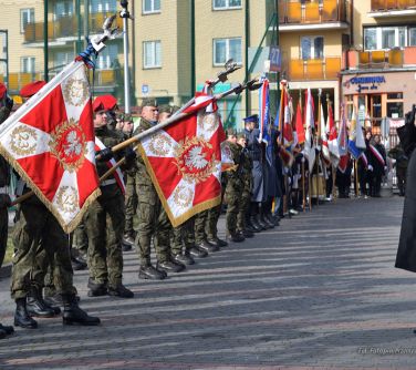 żołnierze trzymaja sztandary, przed nimi salutuje oficer wyższy rangą