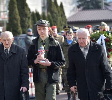 trzy osoby, dwóch mężczyzn, w środku chłopiec   niosący znicz