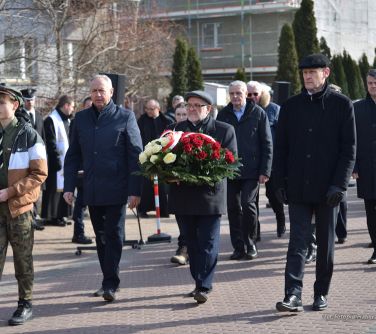 osoby maszerują, w środku mężczyzna niesie bukiet biało-czerwonych kwiatów