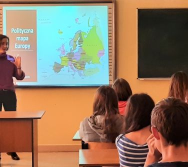 dzieci siedzą w ławkach szkolnych, nauczycielka przemawia do uczniów, w tle wyświetlana mapa polityczna Europy