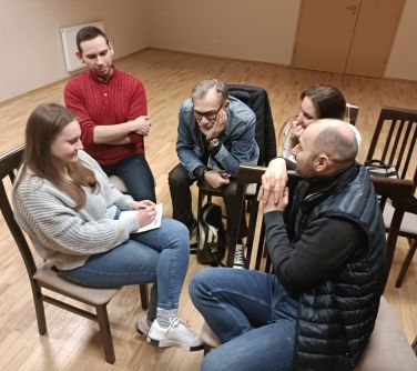 osoby siedzą w kole na krzesłach