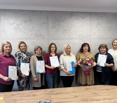 kobiety pozuja do zdjęcia trzymaja w rekach dyplomy, jedna trtzyma bukiet kwiatów