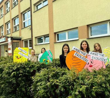 nastolatki stoja w krzakach zielonych trzymają plakaty eco