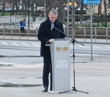 mężczyzna stoi przy mównicy przemawia, mównica stoi na dworze na starym rynku