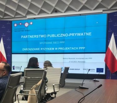 osby siedzą przy stole na konferencji, na tablicy wyświetlono Patnerstwo Publiczno-Prywatne