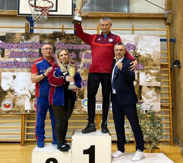 trzech mężczyzn i jedna kobieta pozują do zdjęcia stojąc na podium