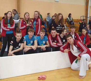 dzieci pozują do zdjęcia na hali sportowej, jeden chłopiec kuca przed białą bandą
