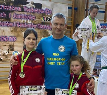 mężczyzna po obu stronach dziewczynki trzymajace dyplomy w dłoniach, na szyi medale
