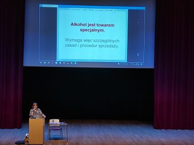 kobieta przemawia do mikrofonu przy mównicy na scenie, w tle ekran