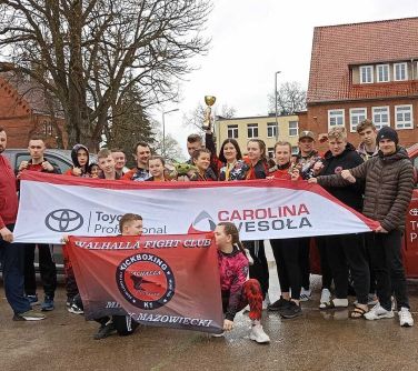 grupa awodników pozuje na tle czerwoego samochodu , przed nimi flagi