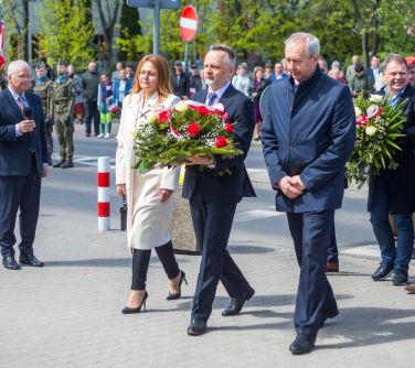 dwóch mężczyzn i kobieta składają wieniec pod pomnik, w tle osoby